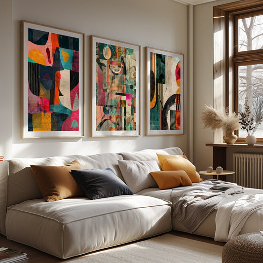 Abstract modern art trio in warm and cool tones, featuring expressive shapes and vibrant colors, displayed on a rustic wall above a minimalist wooden bench with decorative cushions.