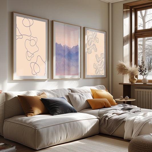 A set of three framed prints: a mountain at sunset and two abstract line art pieces, casting a warm glow in a cozy room.