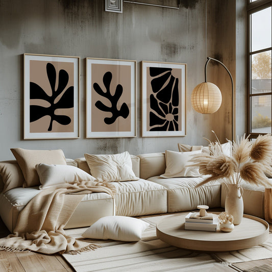 A trio of monochrome leaf prints in bold black and beige, creating an abstract silhouette effect against a contemporary room setting.