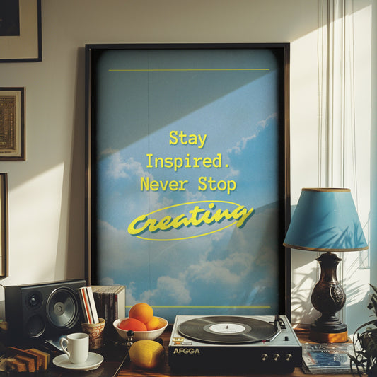 A motivational poster with a background of a blue sky and clouds, featuring the text &quot;Stay Inspired. Never Stop Creating&quot; in vibrant yellow, perfect for inspiring creativity.