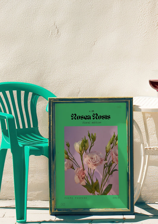 A framed Rosea Rosis poster featuring delicate pink roses on a soft purple background, set against a green frame, displayed in an elegant room with a stylish floor lamp and decorative plants.