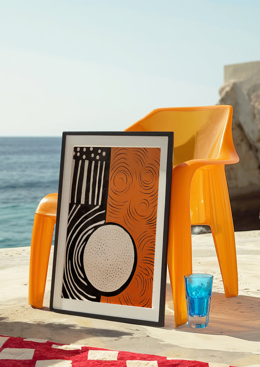 A modern abstract art poster featuring bold geometric shapes in orange and black, leaning against an orange chair by the seaside, creating a striking contrast with the blue ocean background.