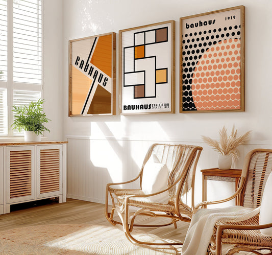 A set of three Bauhaus-inspired posters in neutral tones, featuring geometric designs and bold typography, framed in dark wood, displayed on a light wooden floor against a white wall.