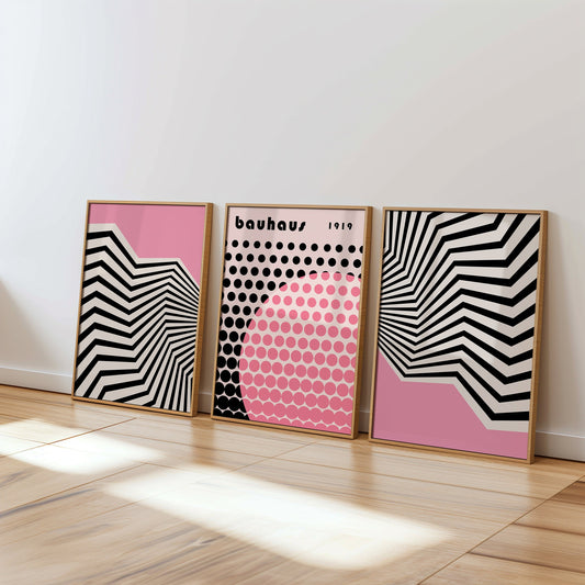 A set of three Bauhaus-inspired geometric posters in pink and black tones, featuring bold striped and dotted patterns, displayed in wooden frames against a clean white wall on a sunlit wooden floor.