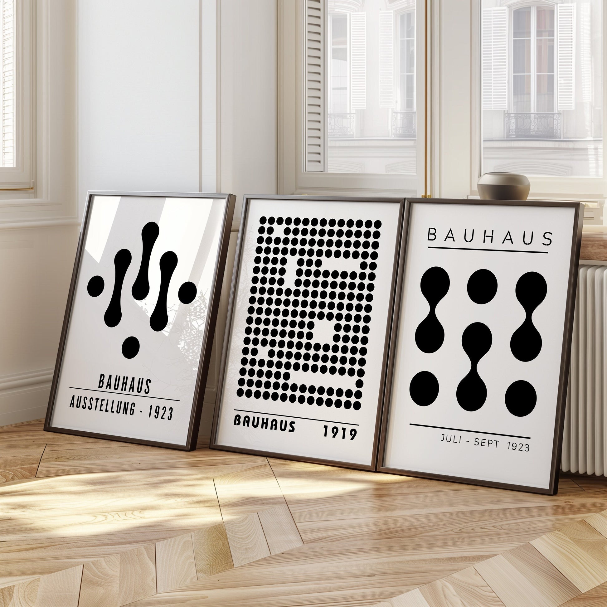 A set of three black and white Bauhaus posters featuring abstract geometric designs, including patterns of dots and organic shapes. The posters are framed and displayed on a light wooden floor, adding a modern and artistic touch to the interior.