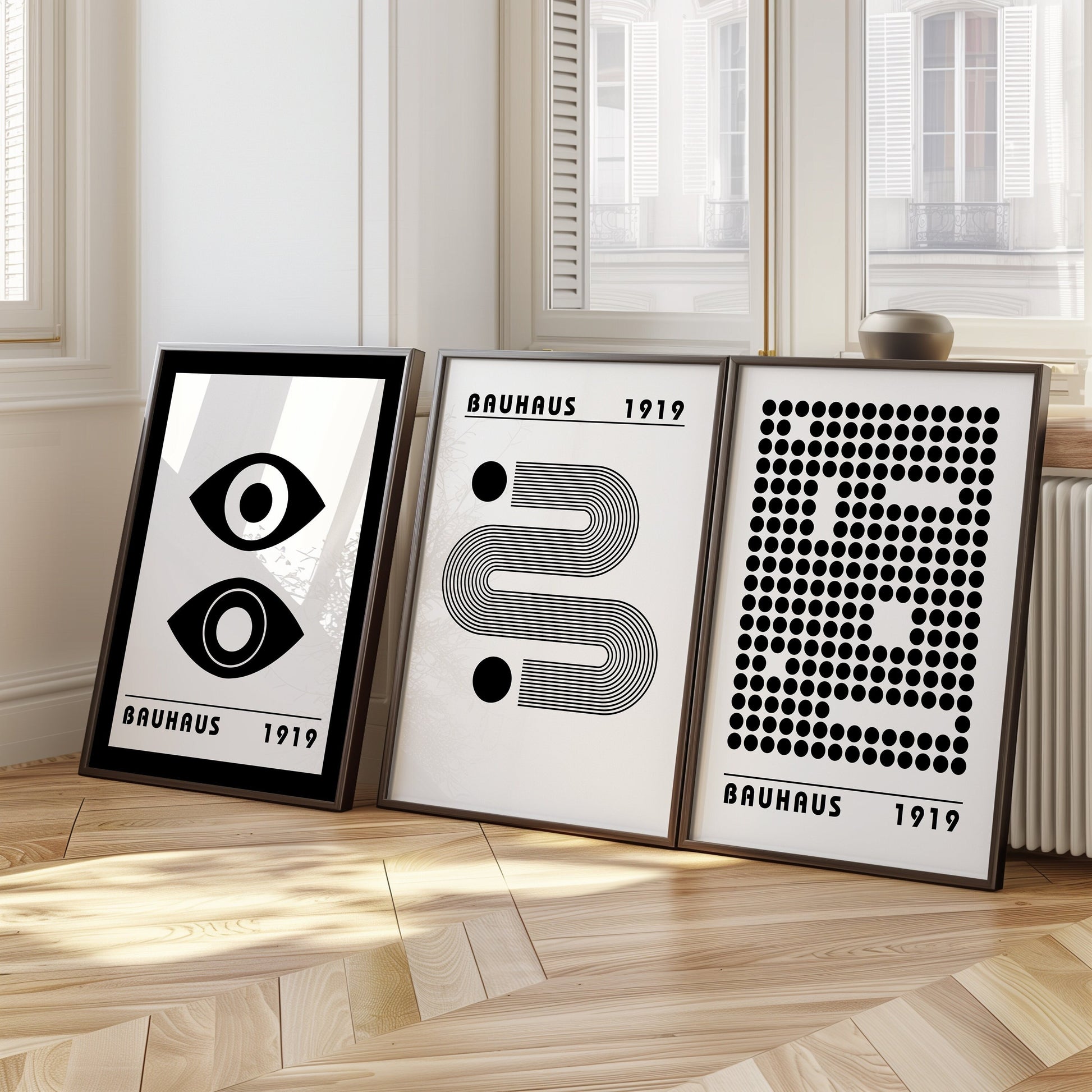 A set of three black and white Bauhaus posters featuring geometric designs and iconic Bauhaus elements, framed in light wood. The posters include a double-eye graphic, abstract lines, and a dotted pattern, perfect for modern minimalist decor.