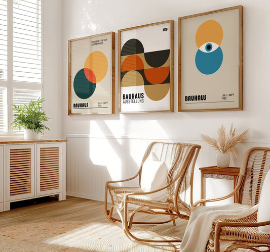 A set of three Bauhaus posters featuring geometric designs with circles and overlapping shapes in orange, blue, black, and green tones, displayed in a minimalist room with wooden flooring.