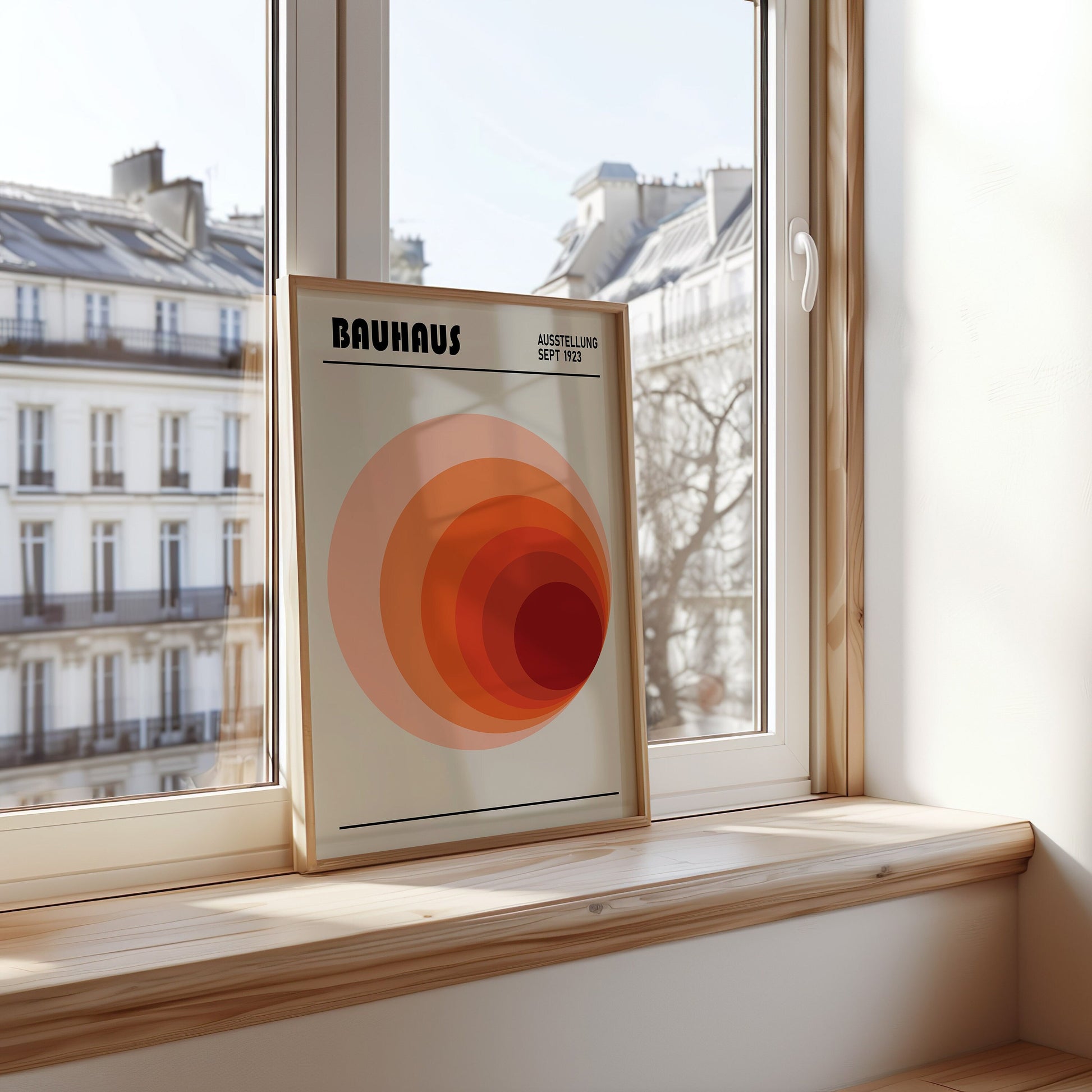 A minimalist Bauhaus poster featuring a red gradient circle design, displayed in a wooden frame against a bright window, perfect for adding modern geometric style to any room.