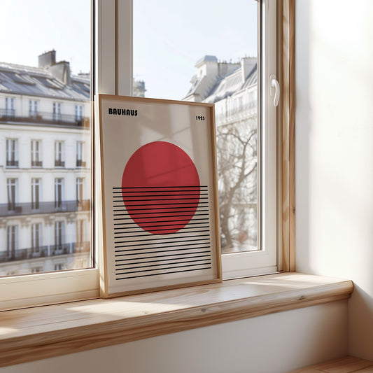 A Bauhaus-inspired art print from 1925 featuring a bold red sun above a series of horizontal black lines, set against a minimalist background, displayed on a windowsill with a view of classic Parisian architecture.