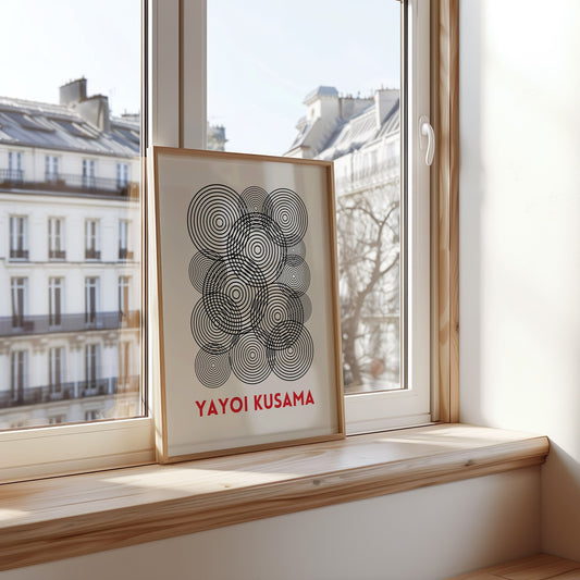 A black and white geometric art print inspired by Yayoi Kusama, featuring a circular design of interwoven lines. The framed poster is placed in a modern kitchen setting, adding a minimalist touch to the space.