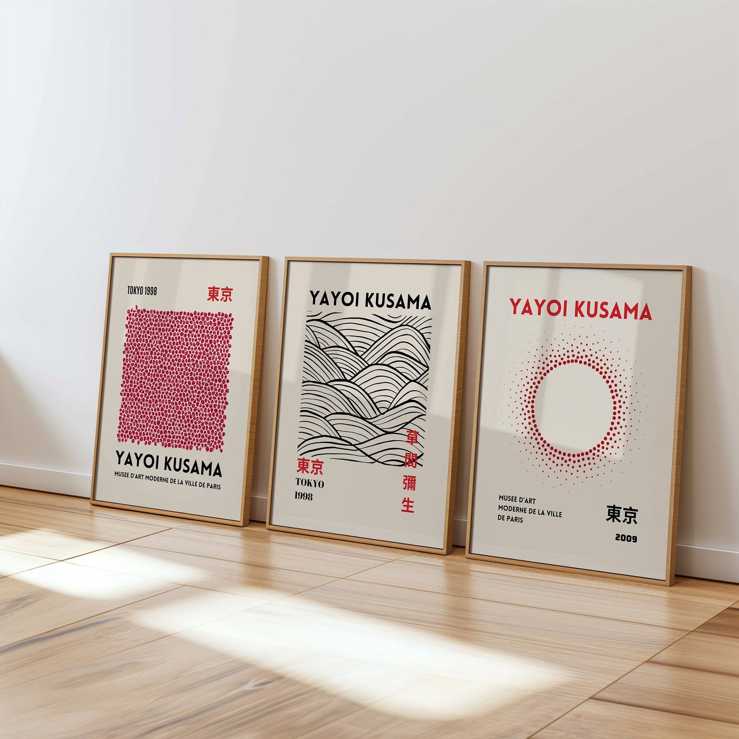 A set of three Yayoi Kusama posters featuring abstract black and white patterns, with dots, waves, and brush strokes, framed in black and placed on a wooden floor.