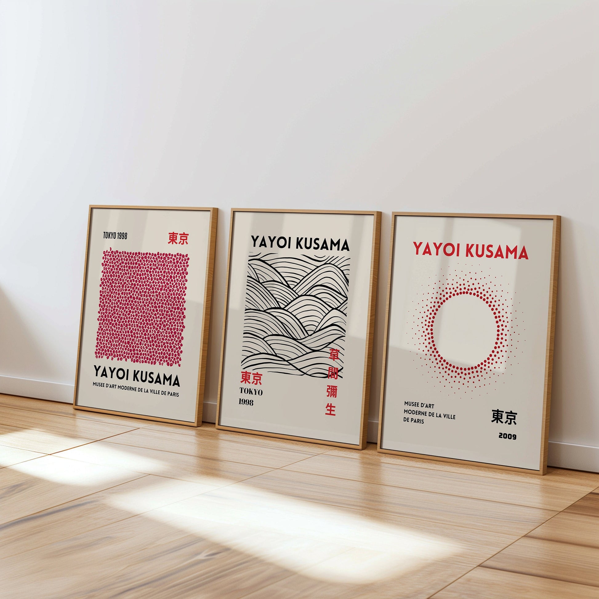 A set of three Yayoi Kusama posters featuring abstract black and white patterns, with dots, waves, and brush strokes, framed in black and placed on a wooden floor.