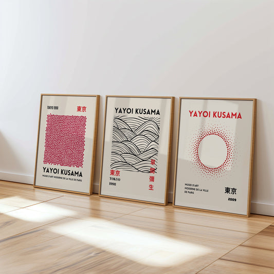 A set of three Yayoi Kusama posters featuring abstract black and white patterns, with dots, waves, and brush strokes, framed in black and placed on a wooden floor.