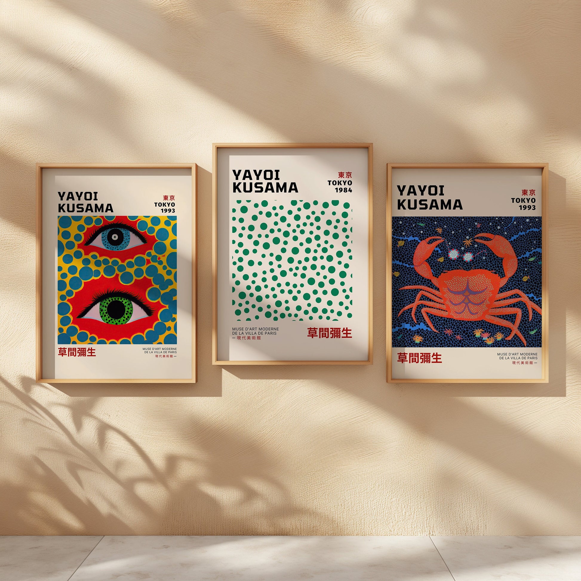 A set of three vibrant Yayoi Kusama posters featuring abstract designs with bold colors, including an eye pattern, a dot pattern, and a crab artwork. Framed and displayed in a bright, airy room with natural light.