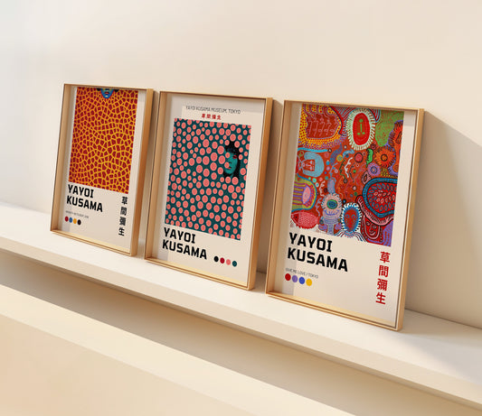 A set of three framed Yayoi Kusama posters displayed on a minimalist shelf. The first poster showcases Kusama&#39;s signature Infinity Nets pattern in orange and yellow hues,