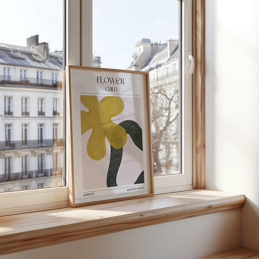 A minimalist poster titled &quot;Flower Child&quot; featuring abstract floral shapes in yellow and green, set against a white background. The gouache-style artwork is framed and displayed on a windowsill with a view of Parisian buildings, creating a serene