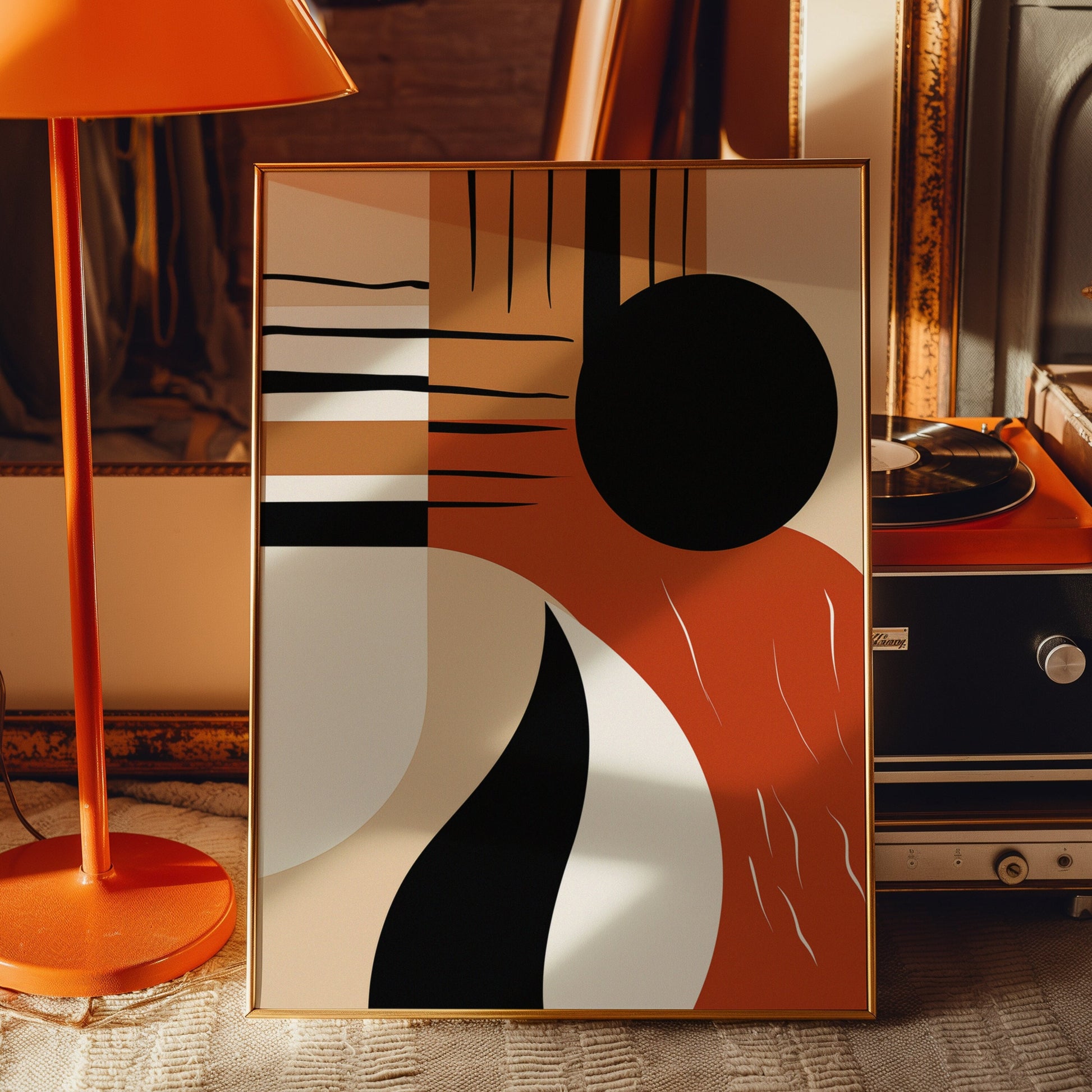 A modern abstract poster featuring minimalist geometric shapes in black, orange, and beige, displayed on a wooden table next to an orange lamp.