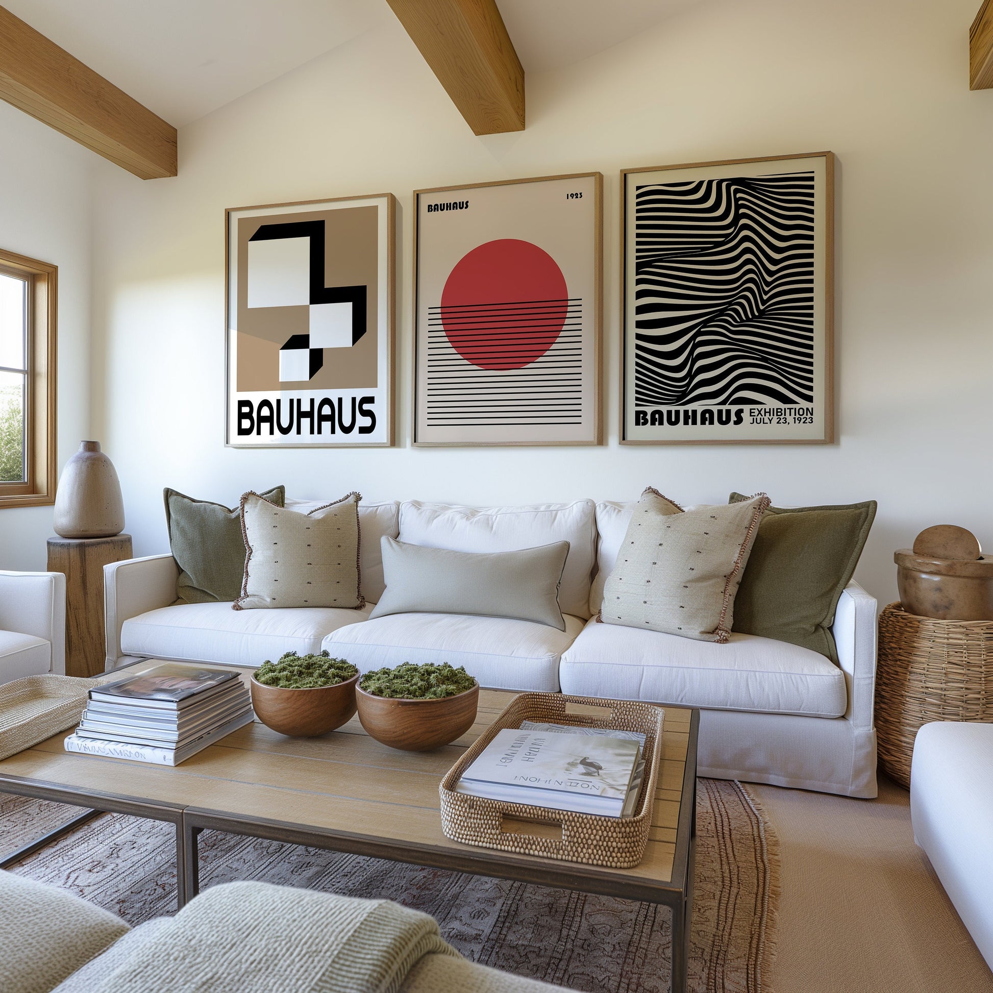 A set of three Bauhaus-inspired posters in black, beige, and red tones, featuring geometric and abstract designs. The framed prints are displayed above a modern white sofa in a cozy living room with natural wood elements.