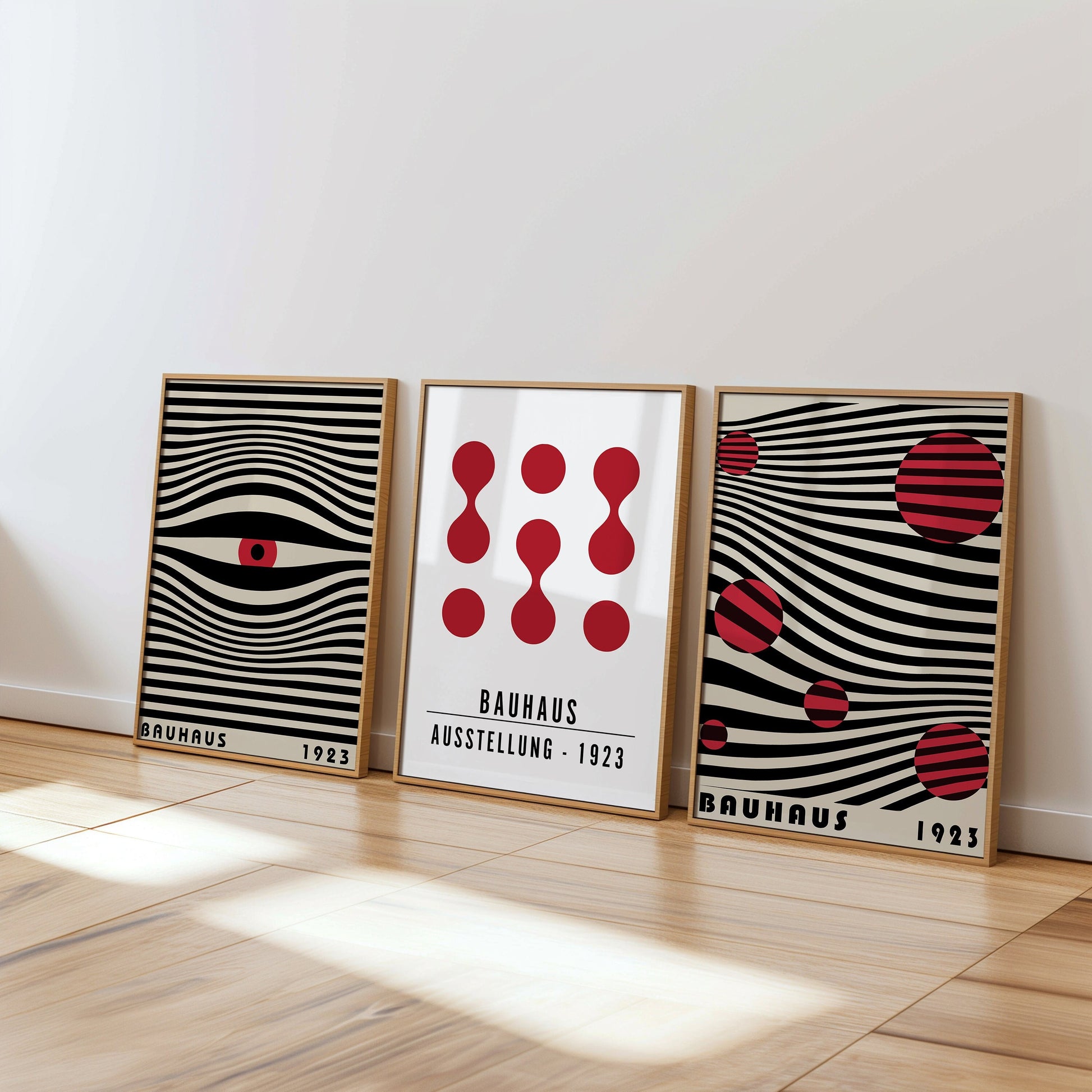 A set of three Bauhaus posters featuring red and black geometric designs on a beige background, framed in light wood and displayed on a modern white shelf. The posters showcase iconic Bauhaus patterns, perfect for adding a touch to any space.