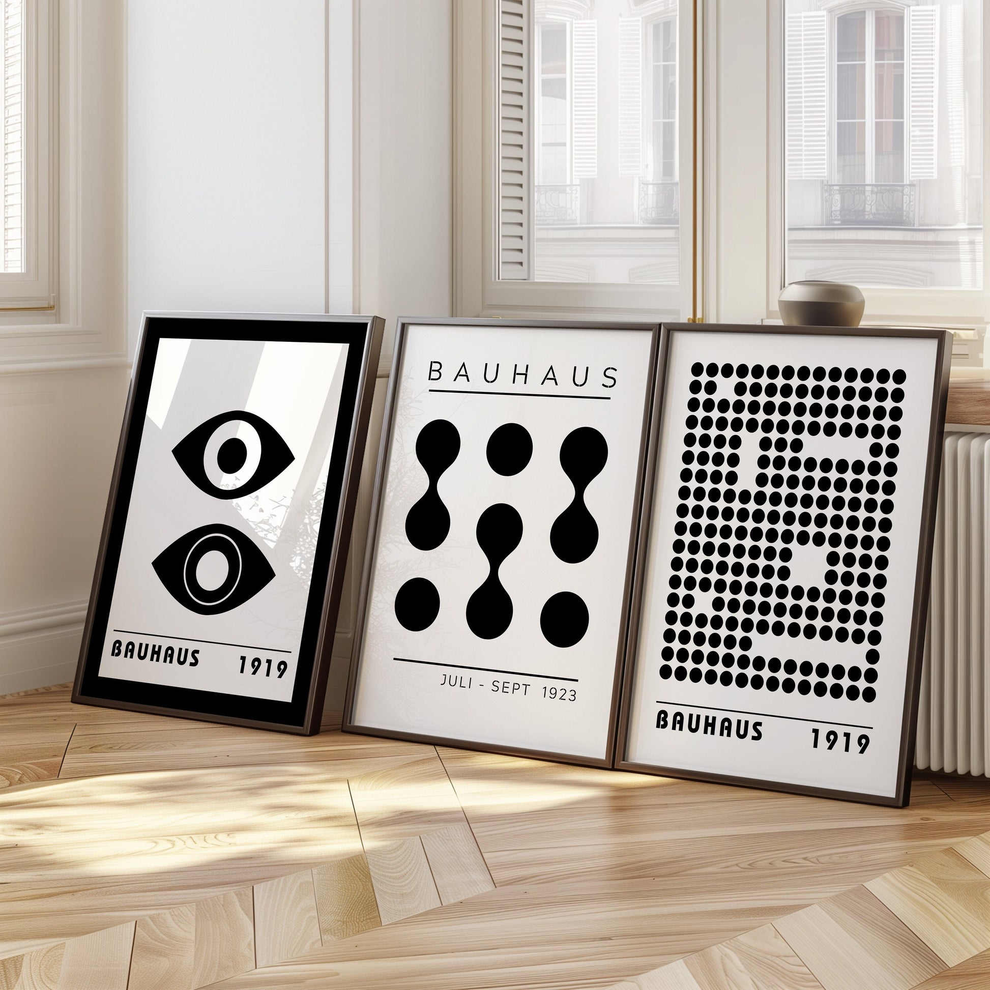 A minimalist set of three Bauhaus posters in black and white, featuring iconic geometric designs from the Bauhaus 1919 and 1923 exhibitions. The set includes an eye graphic, abstract shapes, and a dotted pattern, displayed in a bright, modern room.