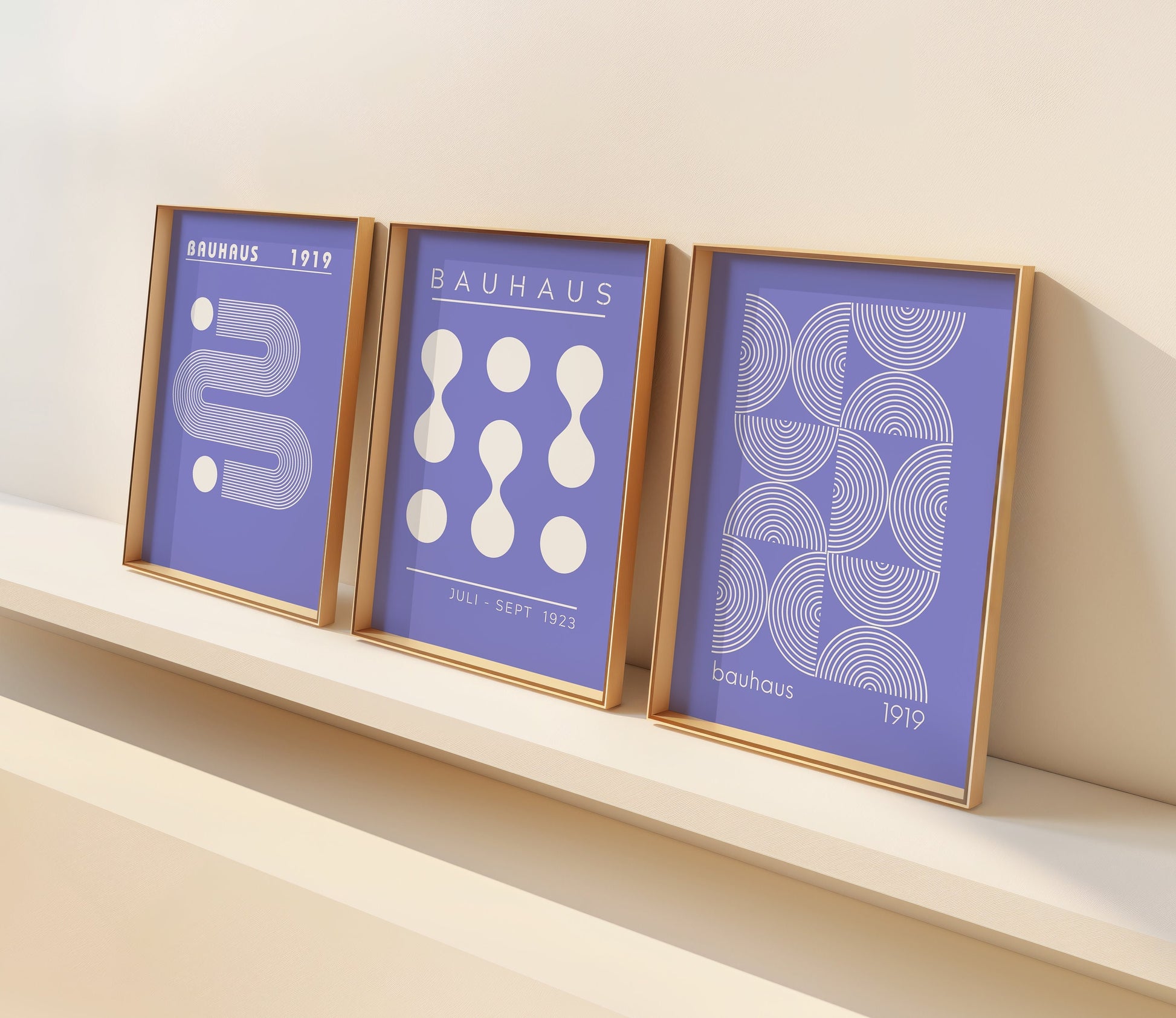 A set of three Bauhaus posters in blue and white, featuring minimalist geometric designs from the 1919 and 1923 Bauhaus exhibitions. Displayed in a modern, bright room with wooden flooring.