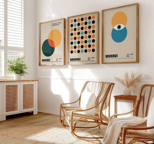 A set of three Bauhaus posters featuring geometric circle designs in orange, blue, black, and yellow. The posters are displayed in a minimalist room with wooden flooring, representing the Bauhaus 1923 exhibition.