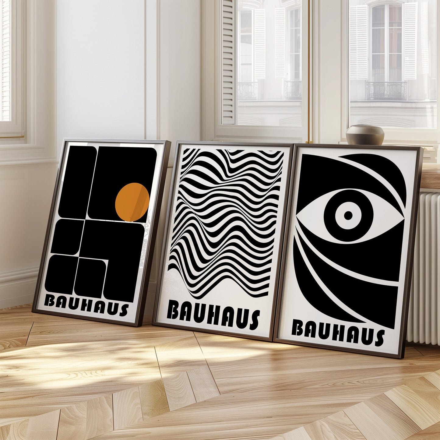 A sleek and modern set of three Bauhaus posters in black and white, featuring minimalist abstract designs with geometric shapes and a striking eye motif. The framed prints are displayed on a wooden floor, adding a bold and artistic touch.