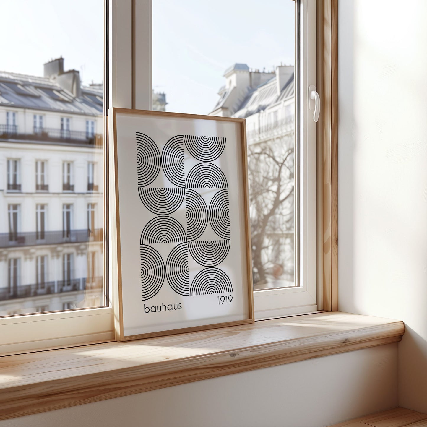 A framed Bauhaus poster with a black and white geometric pattern, leaning against a window in a modern apartment setting. The clean lines and minimalist design make it a perfect addition to any Scandinavian or contemporary decor.