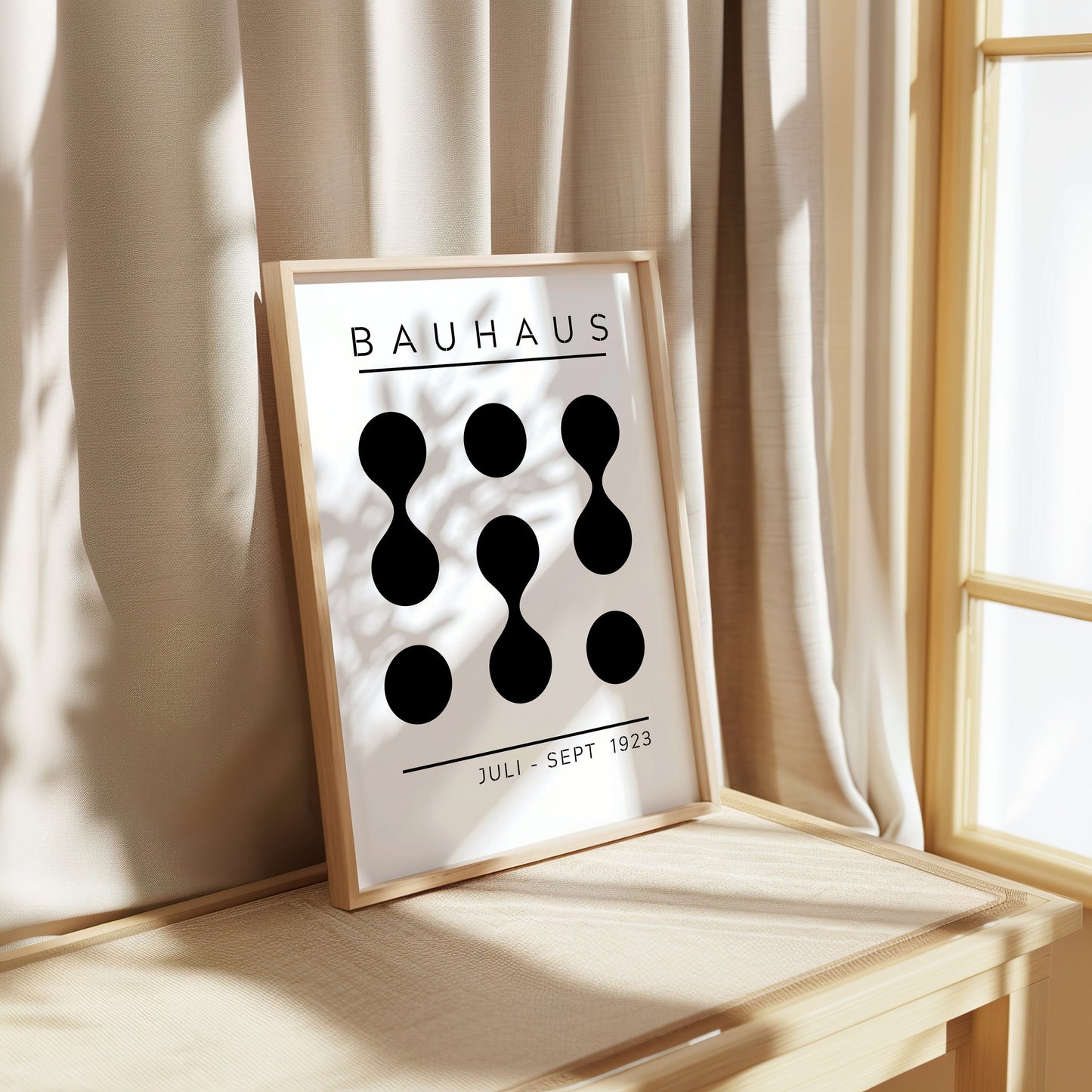 A Bauhaus exhibition poster from Juli-Sept 1923, featuring a minimalist black and white abstract design with geometric shapes, framed and leaning against a beige curtain in a softly lit room.