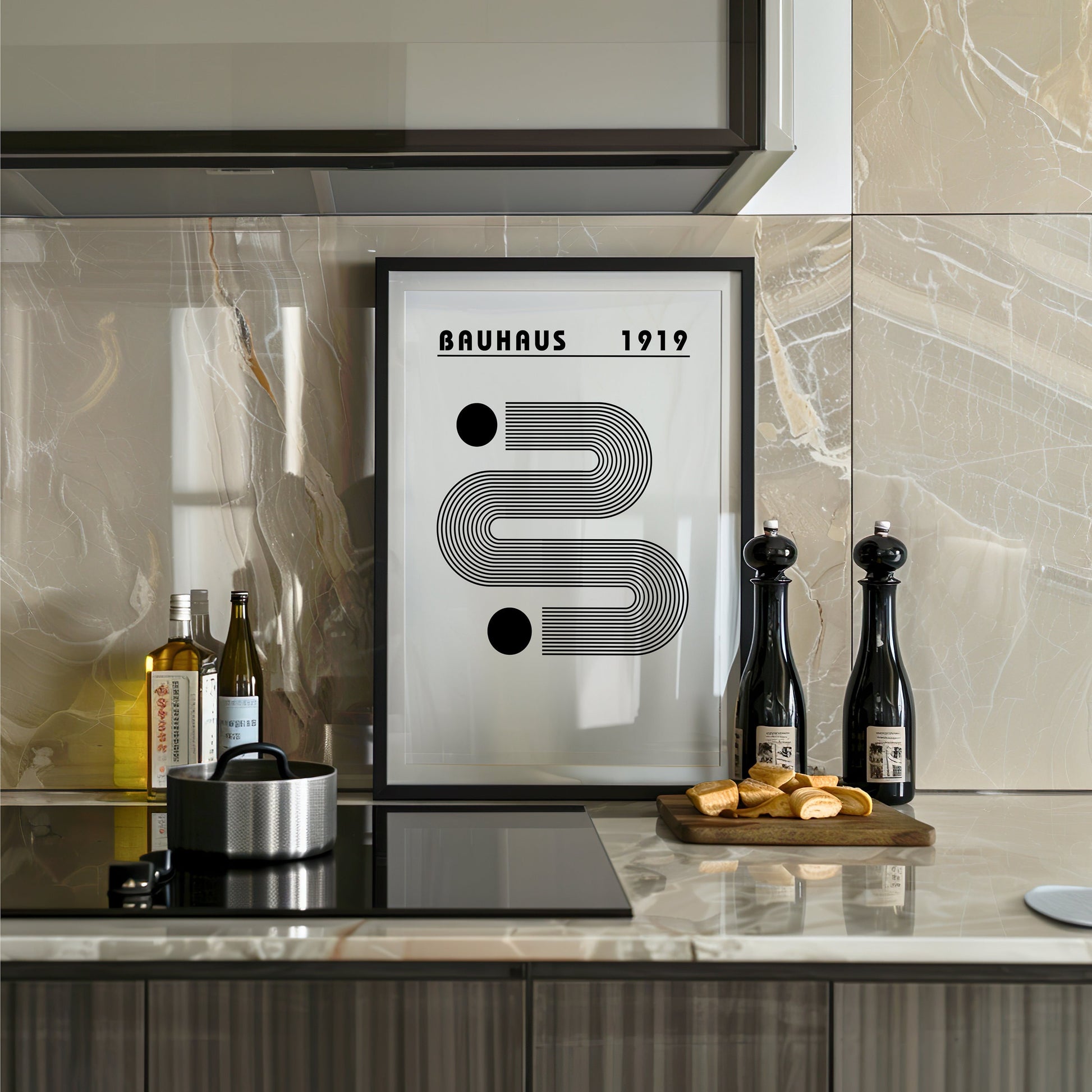 A minimalist Bauhaus 1919 poster with a black and white geometric design, framed and displayed in a modern kitchen setting. The poster is set against a glossy tiled backsplash with bottles and cooking essentials nearby.