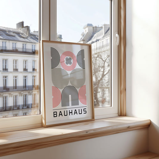 A modern Bauhaus-inspired art print featuring abstract geometric shapes in black, red, and white. The framed print is elegantly displayed on a cozy, textured beige blanket, creating a stylish contrast..