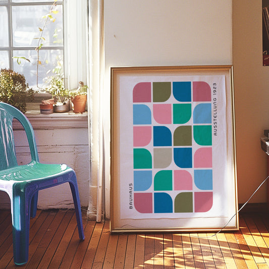 A vibrant Bauhaus-inspired geometric art print featuring a pattern of colorful rounded shapes in green, blue, pink, and teal tones, displayed on a tiled wall with a red door and a blue stool in a modern interior.