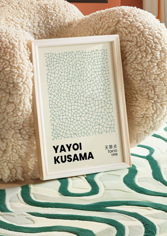 A framed Yayoi Kusama Tokyo 1998 Infinity Nets poster featuring intricate green fine line patterns, displayed on a textured cream chair, adding an artistic touch to any contemporary space.