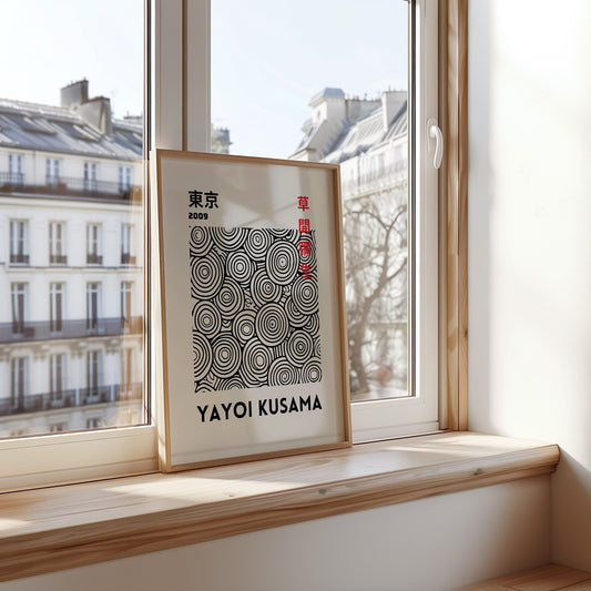 A framed Yayoi Kusama black and white circle art print from Tokyo 2009, displayed on a windowsill with natural light. The abstract poster features concentric circles in black on a white background, adding a modern artistic touch to the interior.