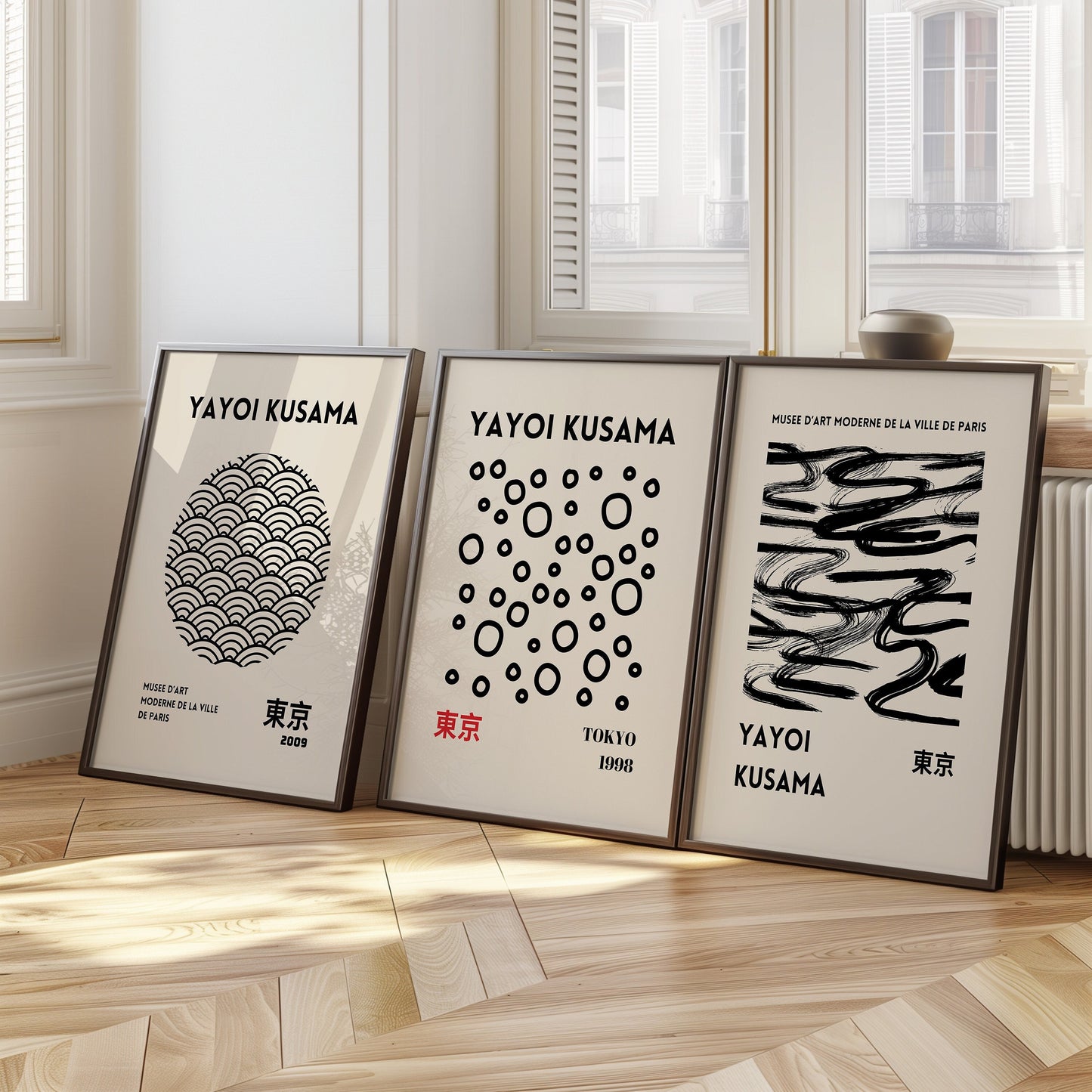 A set of three Yayoi Kusama posters featuring abstract black and white patterns, with dots, waves, and brush strokes, framed in black and placed on a wooden floor.