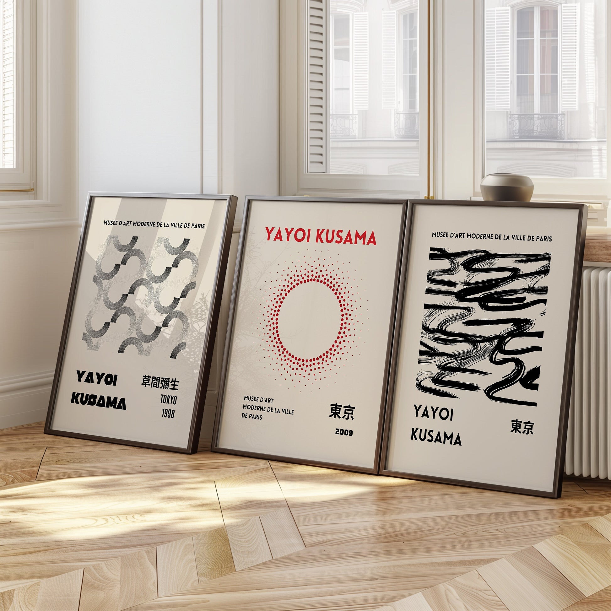 A set of three Yayoi Kusama posters featuring abstract patterns, including circular, fluid, and geometric shapes, framed and displayed on a wooden floor against a bright wall.