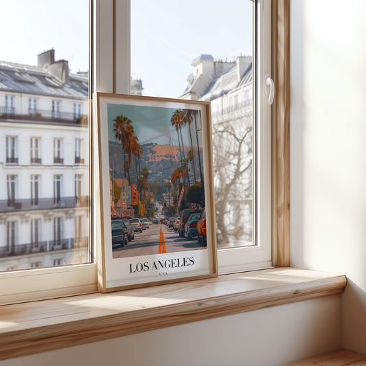 A framed poster showcasing Los Angeles, featuring palm trees, iconic Hollywood hills, and a vibrant city street scene under a bright Californian sky.